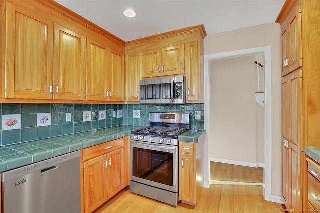 kitchen featuring decorative backsplash, appliances with stainless steel finishes, light wood-type flooring, and tile countertops