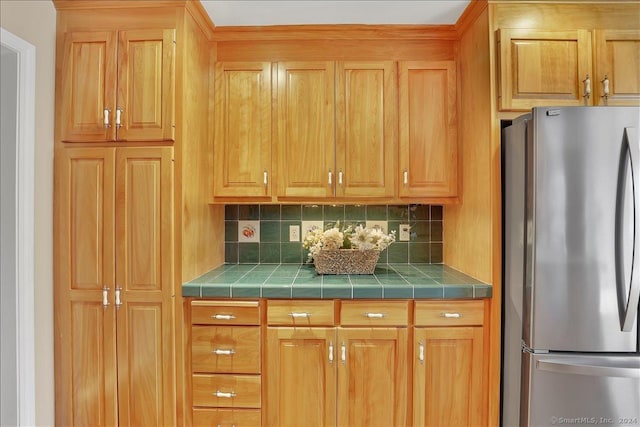 kitchen with tile counters, stainless steel fridge, and backsplash