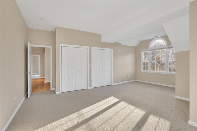 unfurnished bedroom featuring vaulted ceiling, carpet floors, and two closets