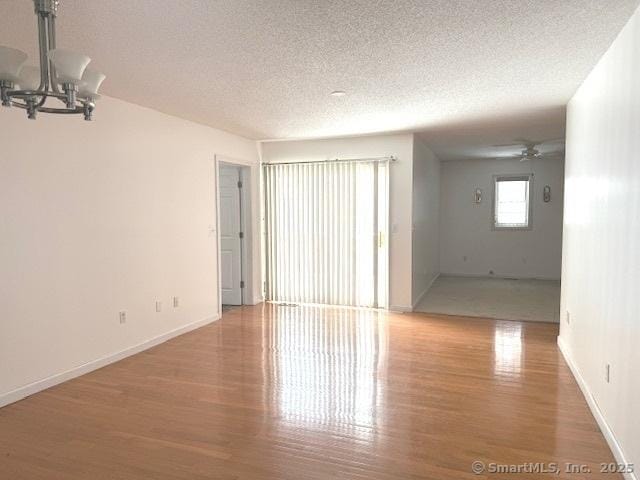 empty room with ceiling fan with notable chandelier, hardwood / wood-style floors, and a textured ceiling