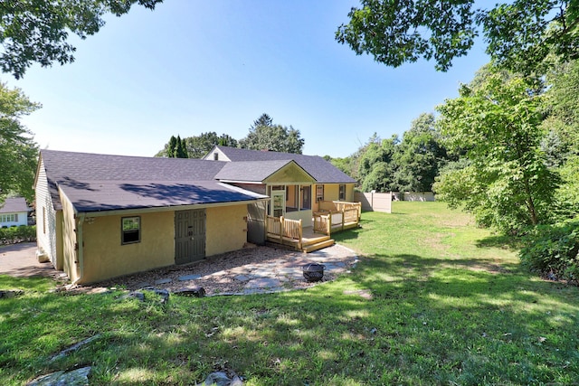 rear view of property with stucco siding, a wooden deck, a yard, and roof with shingles