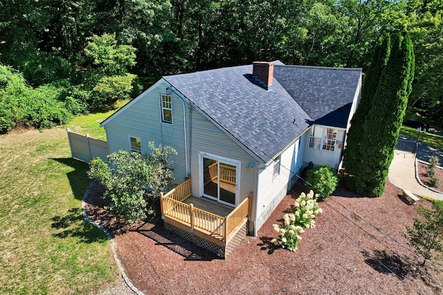 exterior space with a lawn, roof with shingles, a deck, and a chimney