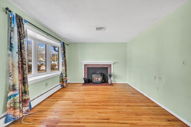 unfurnished living room featuring a baseboard heating unit, light hardwood / wood-style floors, and a wood stove