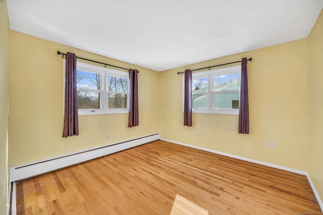 empty room featuring a baseboard heating unit, light hardwood / wood-style flooring, and a healthy amount of sunlight