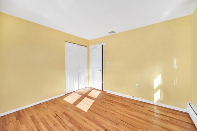 unfurnished room featuring a baseboard heating unit and hardwood / wood-style floors