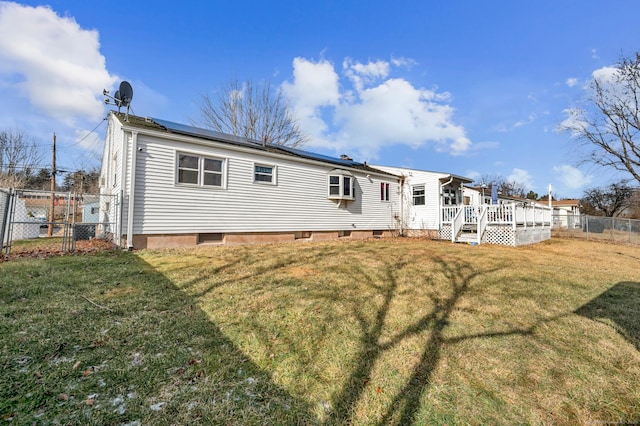 rear view of property with a yard, a deck, and solar panels