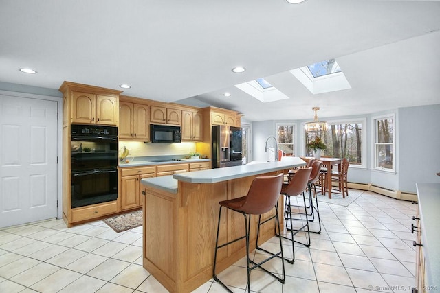 kitchen featuring a baseboard heating unit, lofted ceiling with skylight, decorative light fixtures, a kitchen island with sink, and black appliances