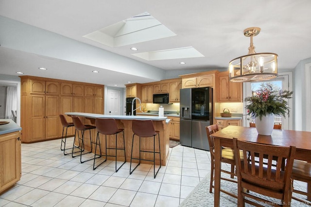 kitchen with a skylight, a chandelier, decorative light fixtures, a kitchen island with sink, and black appliances