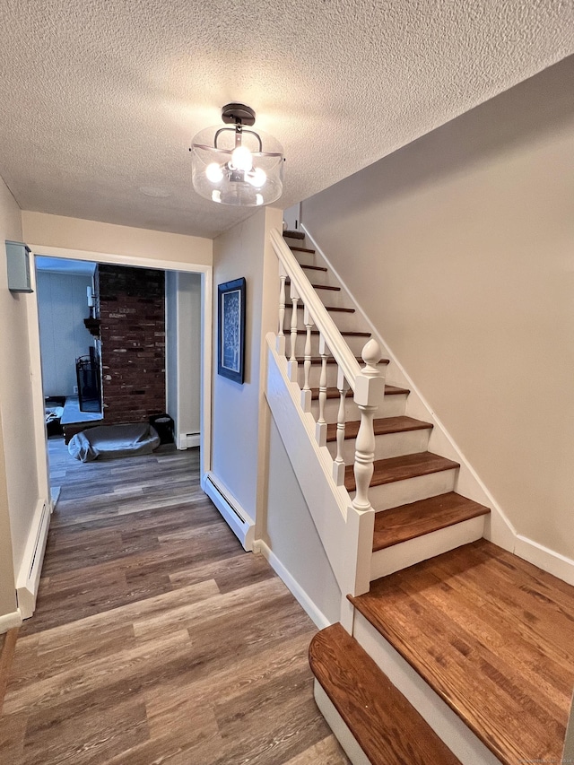 staircase with wood-type flooring, a textured ceiling, and a baseboard heating unit