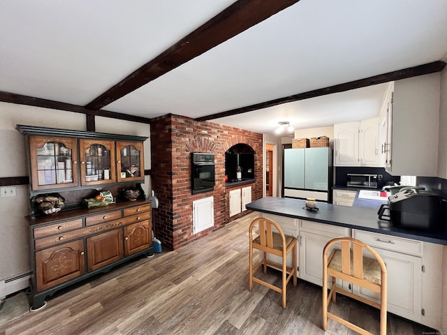 kitchen with dark wood-type flooring, white refrigerator, black oven, white cabinetry, and brick wall