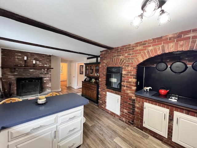 living room featuring brick wall, baseboard heating, beam ceiling, wood-type flooring, and a fireplace