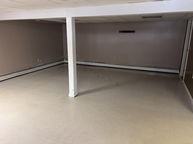 basement featuring a drop ceiling and a baseboard heating unit