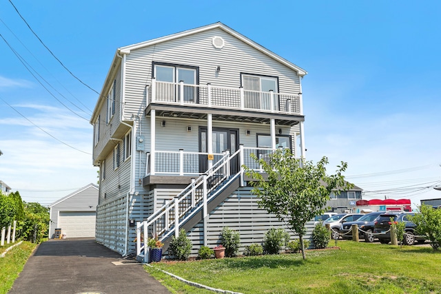 view of front of property featuring covered porch, a front yard, a balcony, a garage, and an outdoor structure