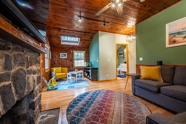 living room featuring ceiling fan with notable chandelier, vaulted ceiling with skylight, wood ceiling, and light wood-type flooring