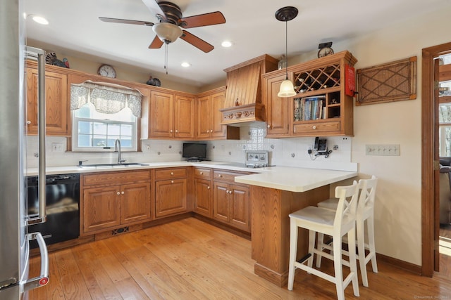 kitchen featuring pendant lighting, black dishwasher, sink, light hardwood / wood-style floors, and kitchen peninsula