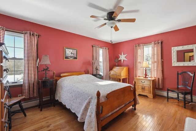 bedroom with multiple windows, hardwood / wood-style floors, ceiling fan, and a baseboard heating unit