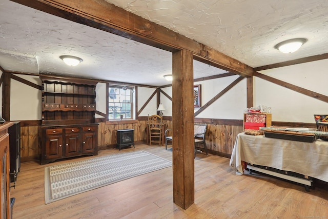 interior space with light wood-type flooring, a wood stove, a textured ceiling, and wood walls