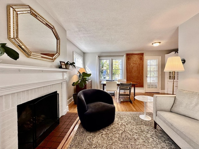 living room with hardwood / wood-style flooring, a textured ceiling, and a brick fireplace