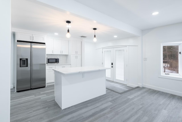 kitchen with white cabinets, appliances with stainless steel finishes, decorative light fixtures, and a kitchen island