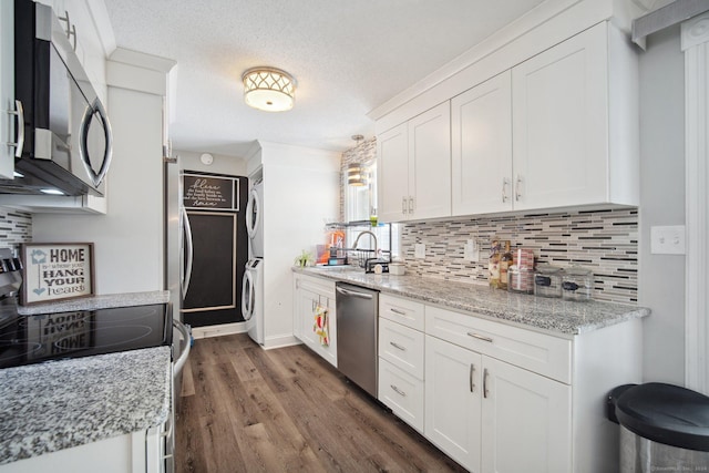 kitchen with stacked washing maching and dryer, stainless steel appliances, white cabinetry, and light stone countertops