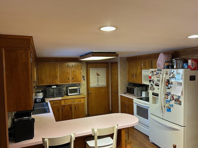 kitchen with kitchen peninsula, a breakfast bar, white appliances, sink, and hardwood / wood-style floors