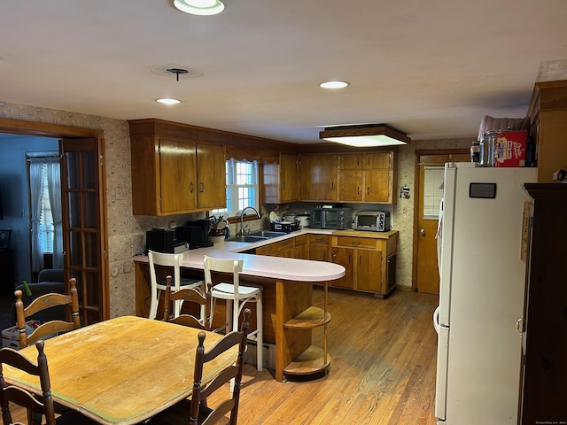 kitchen with kitchen peninsula, decorative backsplash, light hardwood / wood-style floors, sink, and white fridge