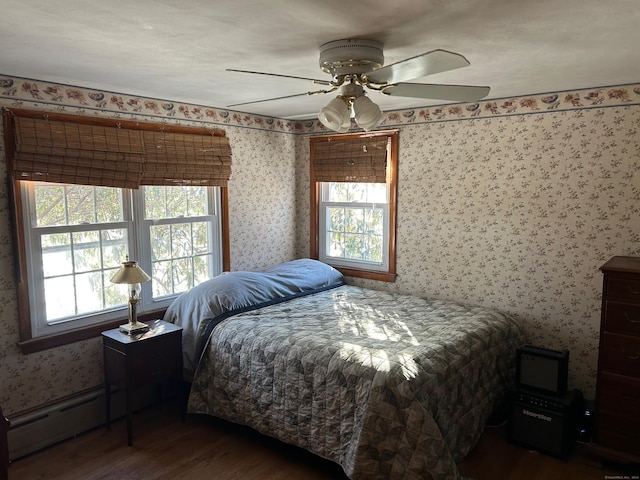 bedroom with multiple windows, dark hardwood / wood-style floors, baseboard heating, and ceiling fan