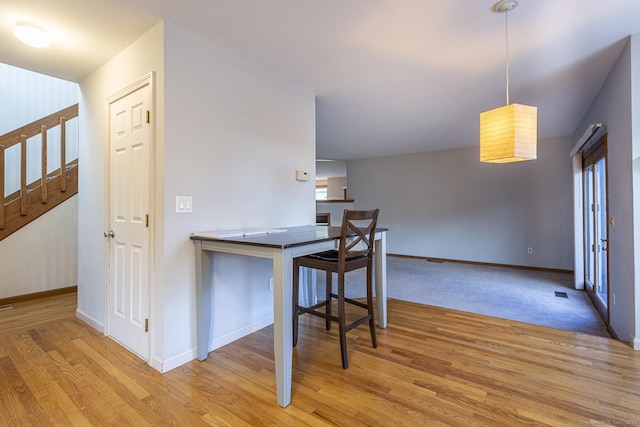 kitchen featuring kitchen peninsula, light wood-type flooring, hanging light fixtures, and a breakfast bar area