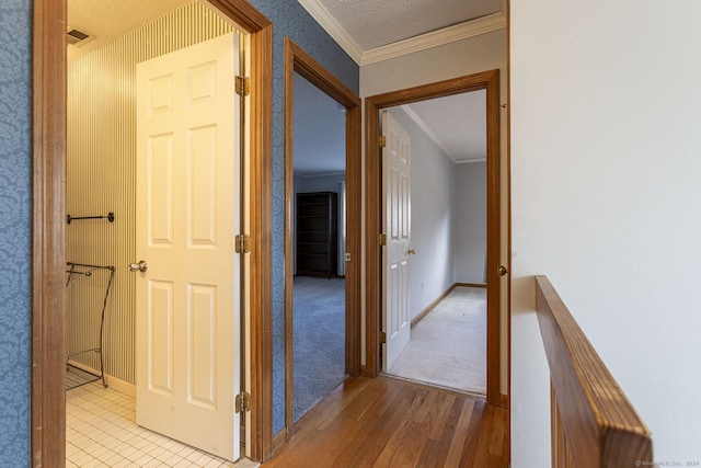 corridor featuring a textured ceiling, light wood-type flooring, and crown molding