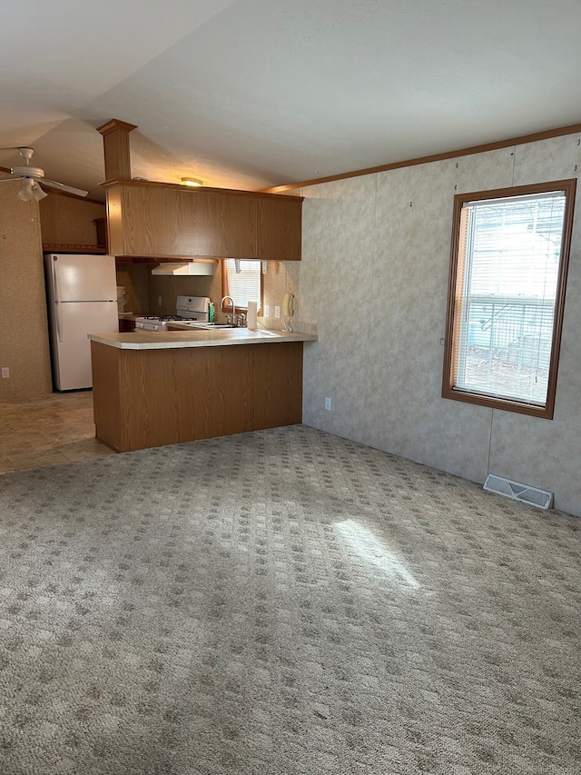 kitchen with carpet floors, white appliances, kitchen peninsula, and vaulted ceiling