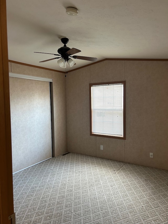 carpeted spare room featuring ceiling fan, lofted ceiling, and ornamental molding