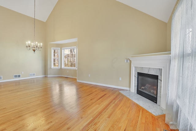 unfurnished living room featuring a high end fireplace, light wood-type flooring, a chandelier, and high vaulted ceiling