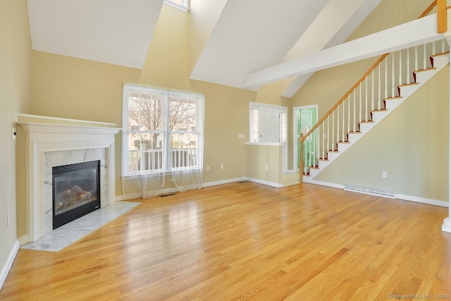 unfurnished living room featuring a premium fireplace, beamed ceiling, high vaulted ceiling, and light wood-type flooring