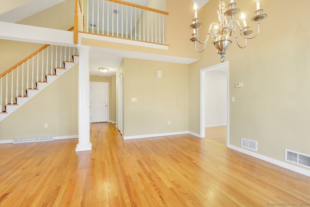 interior space featuring decorative columns, light hardwood / wood-style flooring, a towering ceiling, and a chandelier