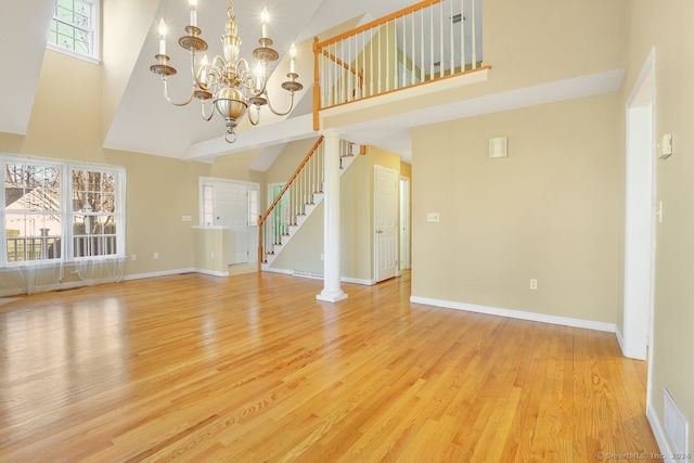 unfurnished living room featuring decorative columns, high vaulted ceiling, light hardwood / wood-style floors, and an inviting chandelier