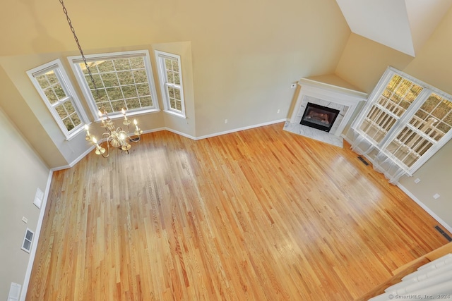 unfurnished living room with a fireplace, an inviting chandelier, high vaulted ceiling, and hardwood / wood-style flooring