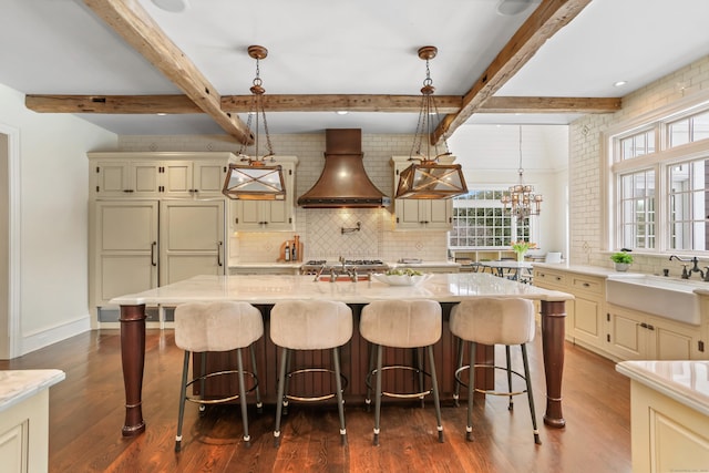 kitchen with sink, custom exhaust hood, decorative light fixtures, a kitchen island, and light stone countertops