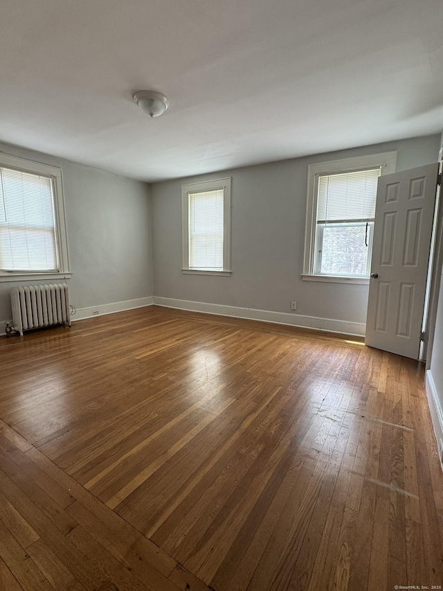 unfurnished room featuring a wealth of natural light, radiator, and hardwood / wood-style floors