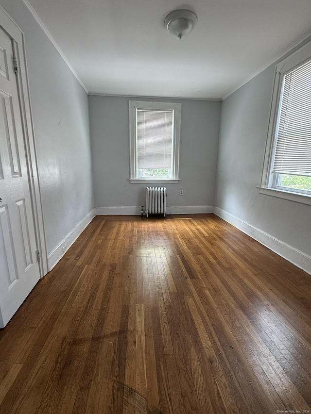 spare room featuring dark hardwood / wood-style flooring, crown molding, radiator, and a healthy amount of sunlight