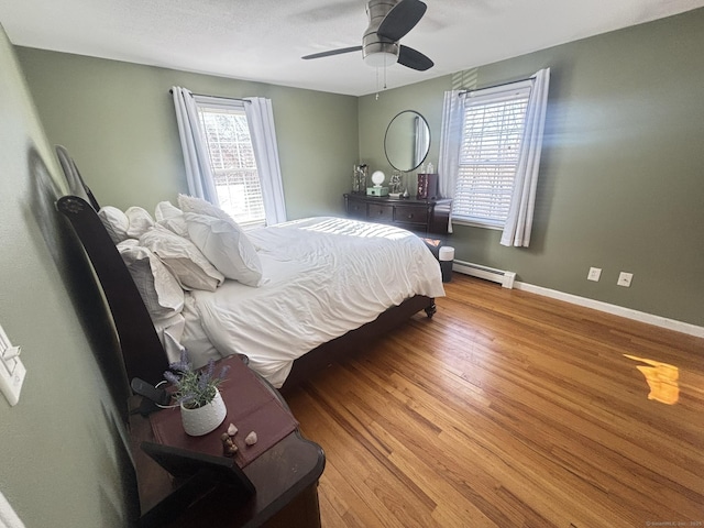 bedroom featuring multiple windows, ceiling fan, wood-type flooring, and a baseboard radiator