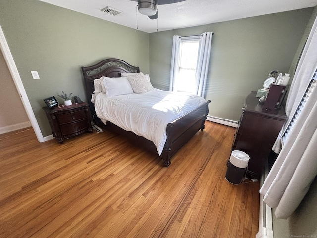 bedroom with ceiling fan, wood-type flooring, and baseboard heating