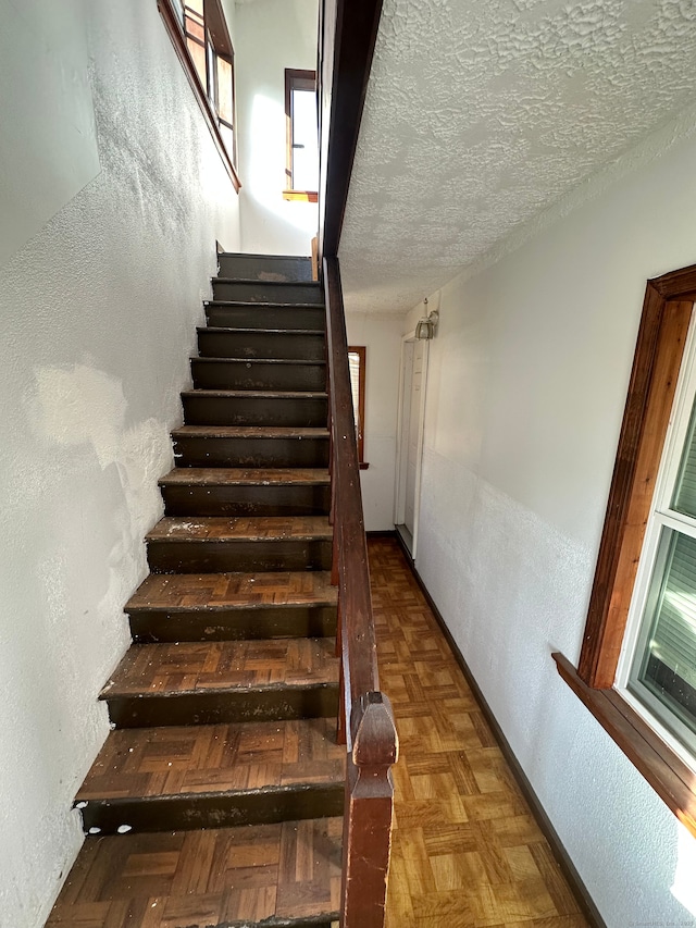 stairway with a textured ceiling and parquet floors