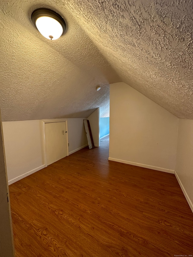 additional living space with a textured ceiling, dark hardwood / wood-style floors, and vaulted ceiling