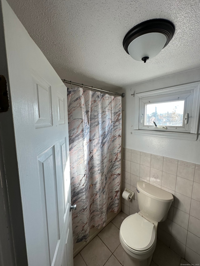 bathroom with toilet, a textured ceiling, tile patterned floors, and tile walls