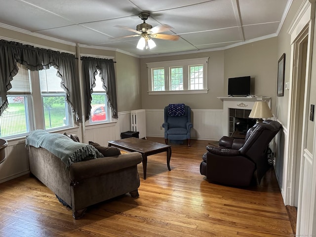 living room featuring radiator heating unit, a tiled fireplace, ceiling fan, crown molding, and light wood-type flooring