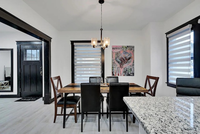 dining space featuring a healthy amount of sunlight, light wood-type flooring, and a notable chandelier