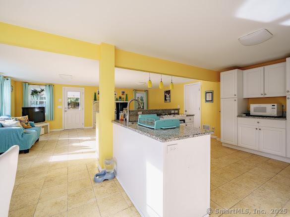 kitchen with white cabinets, light stone countertops, kitchen peninsula, and hanging light fixtures