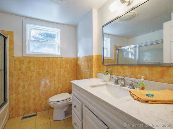 full bathroom featuring vanity, tile patterned floors, toilet, enclosed tub / shower combo, and tile walls