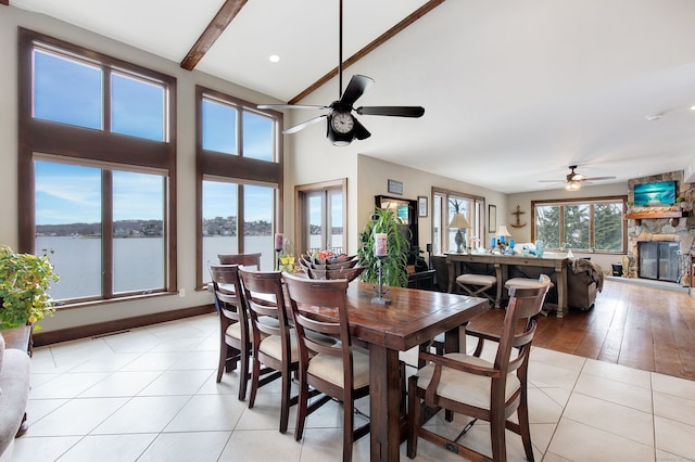 tiled dining room featuring a fireplace, ceiling fan, beamed ceiling, and a water view