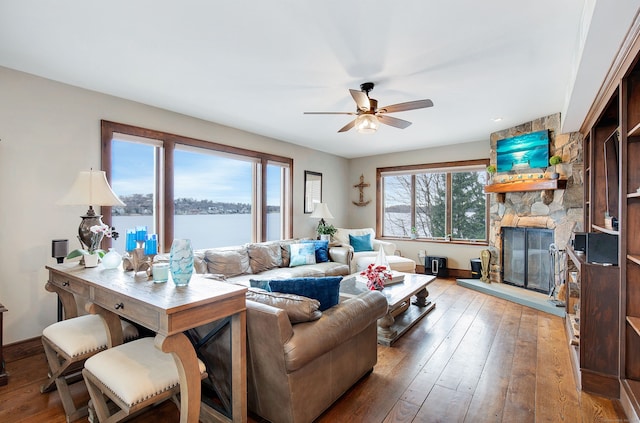 living room with hardwood / wood-style flooring, ceiling fan, and a stone fireplace